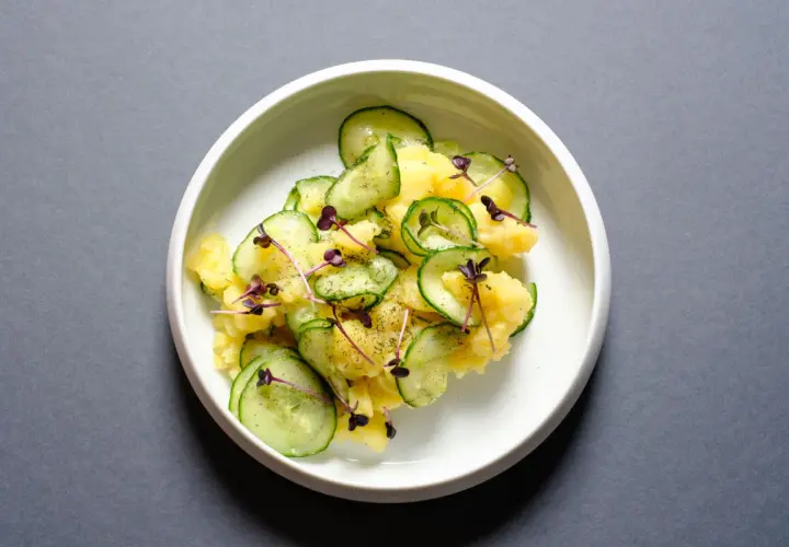 Ein köstlicher Kartoffelsalat mit frischen Gurkenscheiben, garniert mit zarten roten Sprossen und Dill.