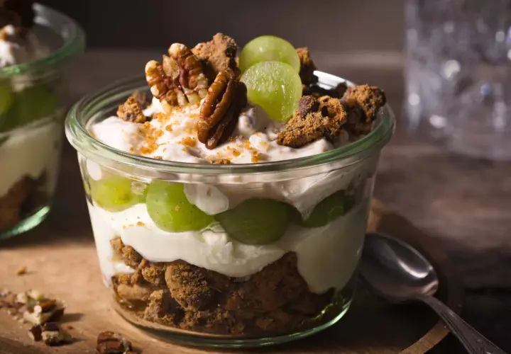 Ein köstliches Dessert im Glas: Schichten aus cremigem Joghurt, saftigen Weintrauben und knusprigen Cookie-Stücken, garniert mit Pekannüssen.