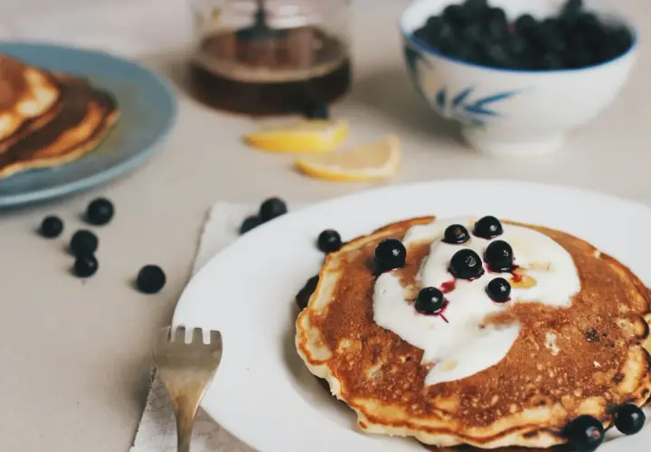 Leckere Pfannkuchen ohne Ei, garniert mit Joghurt und Blaubeeren, serviert mit Honig und Zitronenspalten.