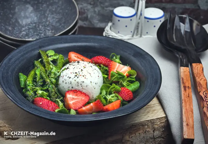 Ein frischer Spargelsalat mit Erdbeeren und Burrata, garniert mit Kräutern und Pfeffer.