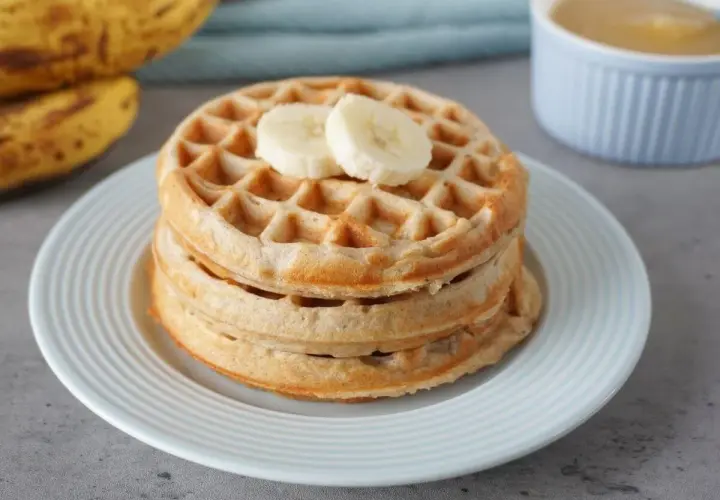 Stapel goldbrauner bananenwaffeln ohne zucker, garniert mit Bananenscheiben. Daneben liegen reife Bananen.