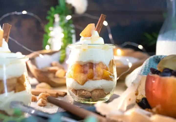 Leckeres Apfel-Crumble-Dessert im Glas mit Zimtstange und Sahne. Ein süßer Genuss, der zum Naschen einlädt.
