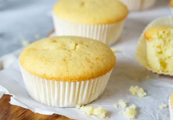 Frisch gebackene Vanille-Muffins, perfekt für ein einfaches Muffins Rezept. Einer ist angeschnitten und zeigt die saftige Krume.