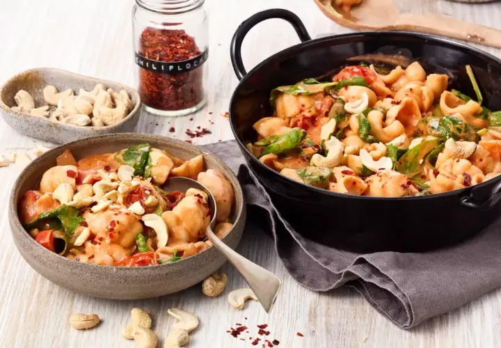 Ausgefallene Pasta-Rezepte vegetarisch: Cremige Muschelnudeln mit Cashews, Tomaten und Spinat, bestreut mit Chili-Flocken.