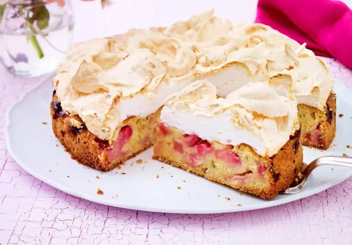 Ein saftiger Rhabarberkuchen mit einer luftigen Baiserhaube, auf einem weißen Teller angerichtet.