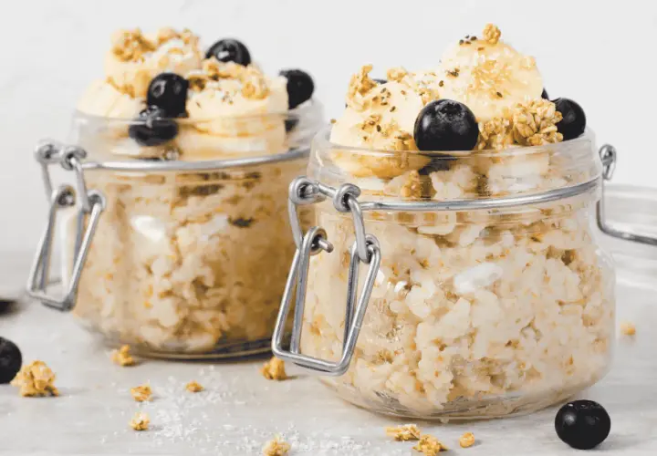 Zwei Gläser mit Overnight Oats, garniert mit Bananenscheiben, Blaubeeren und Granola. Perfekt für ein schnelles Frühstück.