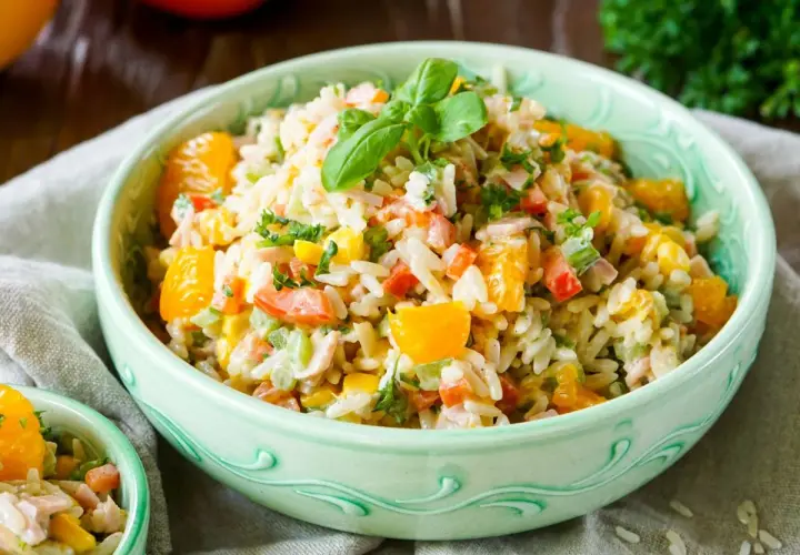 Erfrischender Reissalat mit Mandarinen, Paprika, Mais und Kräutern, garniert mit Basilikum.