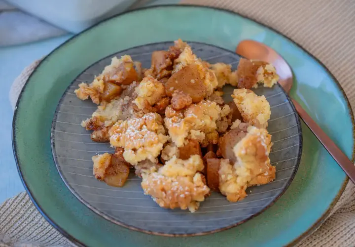 Ein Teller mit warmem Apfel Crumble, bestäubt mit Puderzucker. Die goldbraunen Apfelstücke und knusprigen Streusel laden zum Genießen ein.
