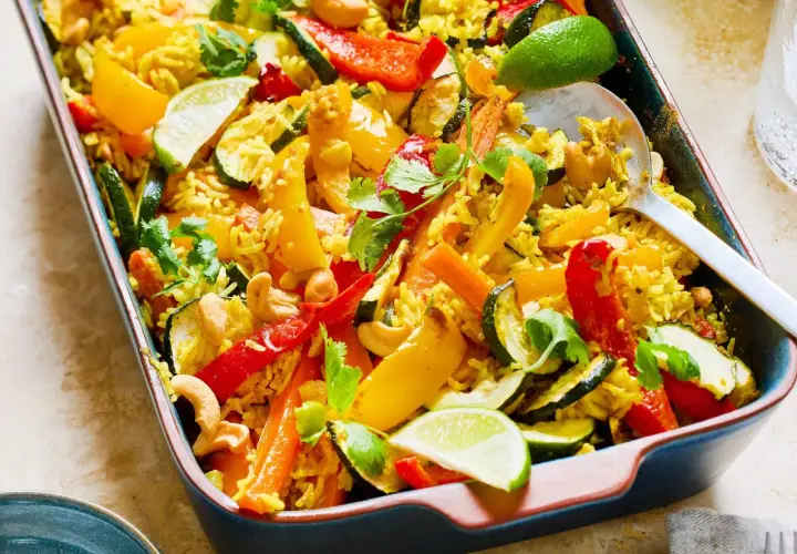 Buntes Gericht mit Reis, Paprika, Zucchini, Karotten und Cashewkernen, garniert mit Koriander und Limettenspalten. Ein köstliches Gericht mit Reis.