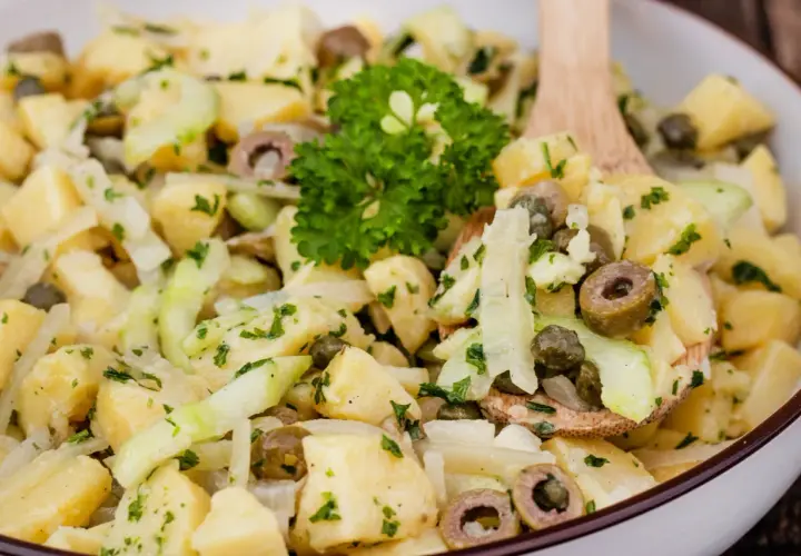 Ein köstlicher Kartoffelsalat ohne Mayo mit Gurken, Oliven und Kapern, garniert mit Petersilie.