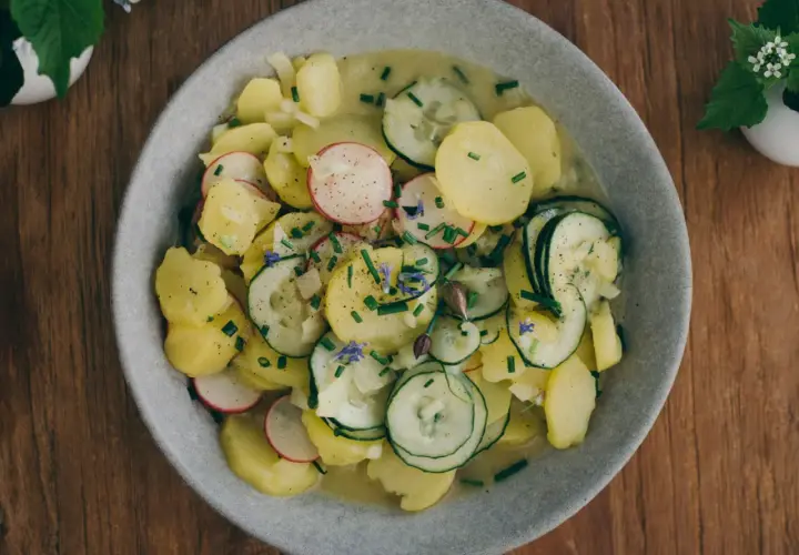 Bayrischer Kartoffelsalat mit Speck und Zwiebeln, garniert mit Radieschen, Gurken und Schnittlauch. Ein deftiger Genuss!