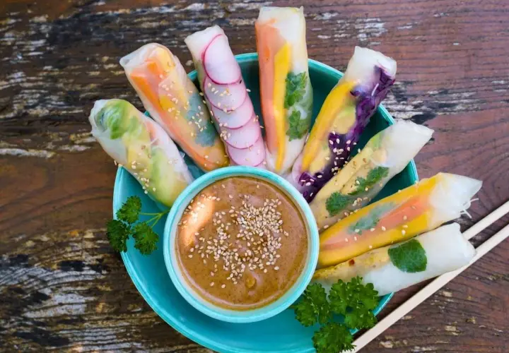 Frische Sommerrollen mit bunten Gemüsesorten, garniert mit Sesam, serviert mit Erdnussdip. Perfekt für ein leichtes Sommerrollen Rezept.