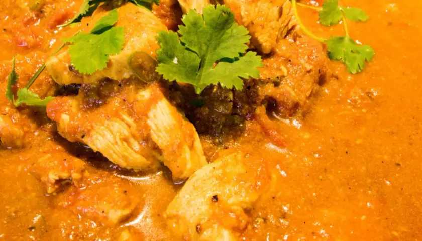 Ein köstliches indisches Curry Rezept mit zarten Hähnchenstücken in einer cremigen Tomaten-Currysauce, garniert mit frischem Koriander.