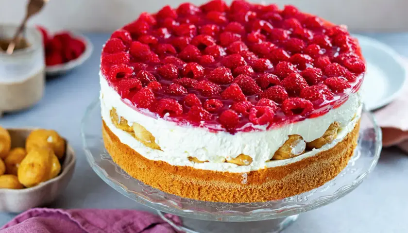 Eine köstliche Windbeuteltorte mit Himbeeren, geschichtet mit Sahne und Biskuit, verlockt zum Genuss.