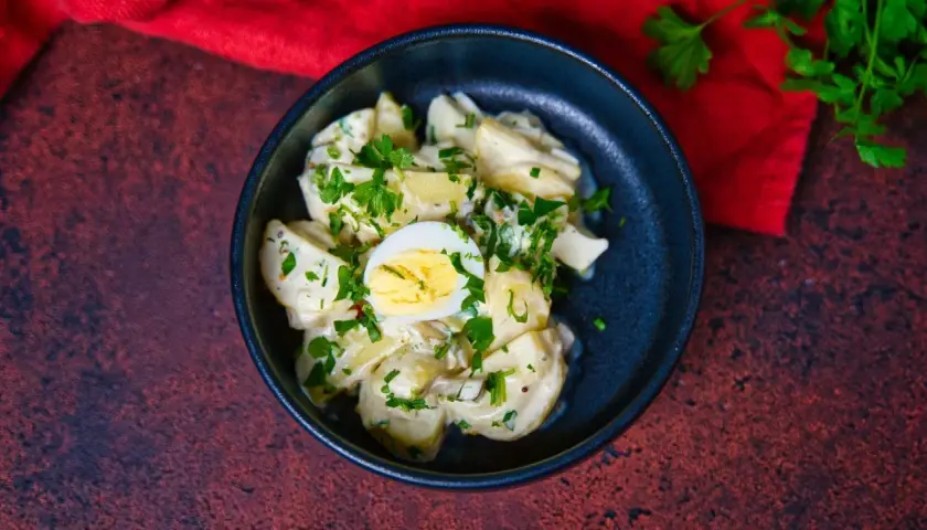 Ein cremiger Kartoffelsalat mit Mayo, garniert mit Petersilie und einem halben Ei. Perfekt für ein Picknick!