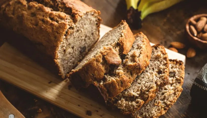 Ein saftiges Bananenbrot, perfekt für ein Bananenbrot Rezept ohne Zucker. Daneben liegen Mandeln und reife Bananen.