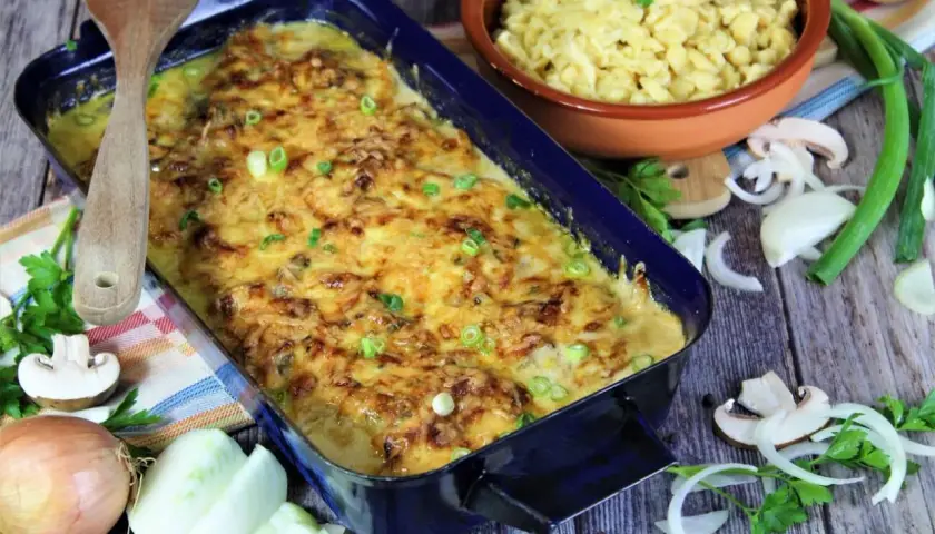 Herzhaftes Zwiebel Sahne Schnitzel mit Käse überbacken, daneben Spätzle und frische Zutaten.