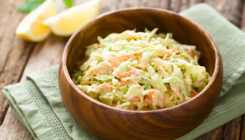 Cremiger Krautsalat mit Karotten, perfekt für jedes BBQ. Ein einfaches coleslaw rezept, das immer gelingt. Serviert in einer Holzschale mit Zitronenspalten.