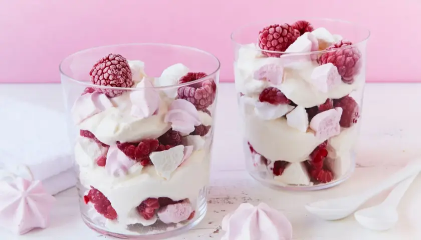 Zwei Gläser mit Himbeer Baiser Dessert, geschichtet mit Sahne, frischen Himbeeren und zarten Baiserstückchen.