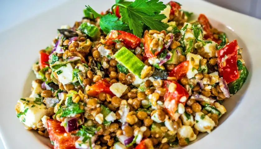 Ein bunter Linsensalat mit Feta, Gurken, Tomaten und roten Zwiebeln, garniert mit Petersilie.