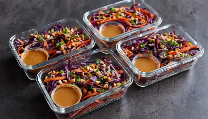 Vier Glasbehälter mit einem bunten Salat aus Rotkohl, Karotten und Erdnüssen. Perfekt für Rezepte mit viel Protein und wenig Kalorien.