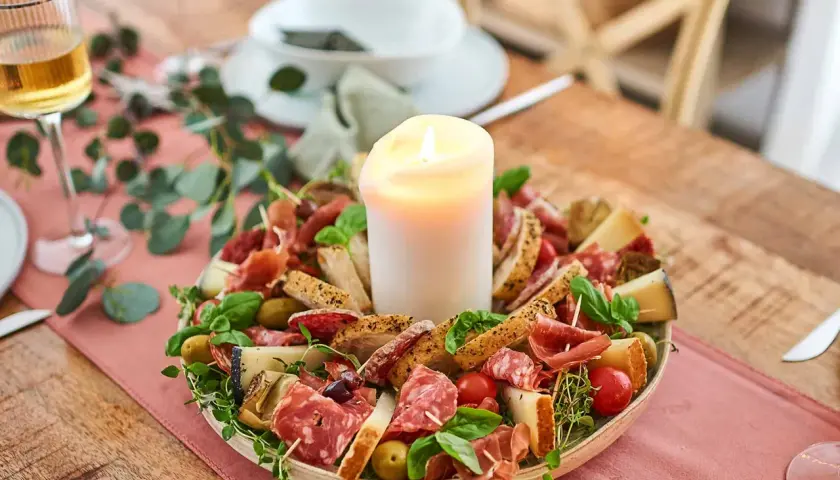 Eine festliche Platte mit Wurst, Käse, Brot und Oliven, die zum Antipasti selber machen einlädt. Ein Kerzenlicht sorgt für Gemütlichkeit.