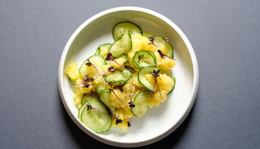 Ein köstlicher Kartoffelsalat mit frischen Gurkenscheiben, garniert mit zarten roten Sprossen und Dill.