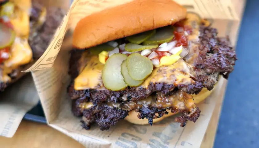 Saftige Burger-Patties mit geschmolzenem Käse, Gurken und Zwiebeln auf einem Brötchen, serviert auf Zeitungspapier.