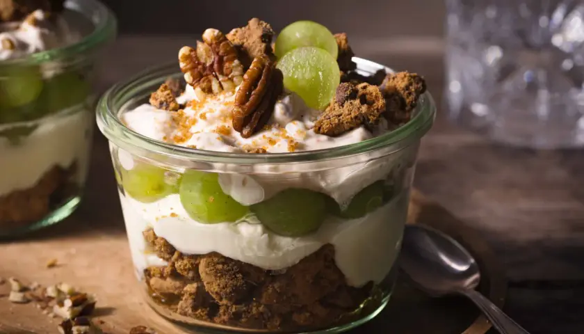 Ein köstliches Dessert im Glas: Schichten aus cremigem Joghurt, saftigen Weintrauben und knusprigen Cookie-Stücken, garniert mit Pekannüssen.