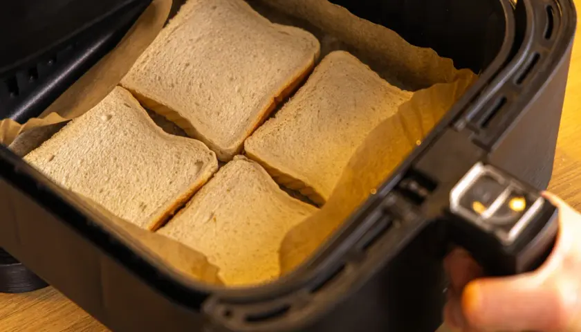 Vier Scheiben Toastbrot liegen in der Schublade eines Airfryers, bereit für ein schnelles Toast Hawaii.