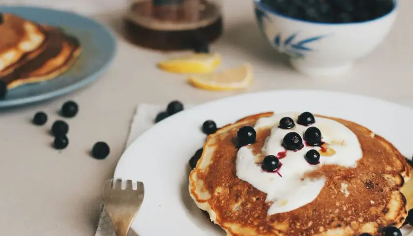 Leckere Pfannkuchen ohne Ei, garniert mit Joghurt und Blaubeeren, serviert mit Honig und Zitronenspalten.