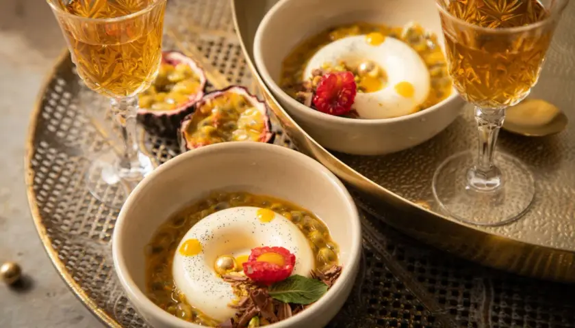 Zwei Panna Cotta-Desserts, inspiriert vom original italienischen Rezept, serviert mit Passionsfrucht und einem Hauch von Himbeere.