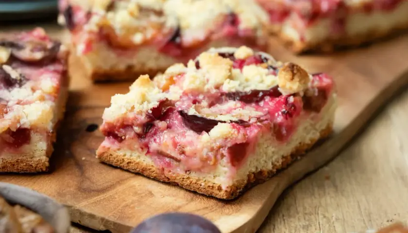 Saftiger Zwetschgenkuchen mit Streuseln auf einem Holzbrett. Ein Stück ist angeschnitten und zeigt die saftigen Früchte.
