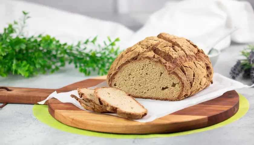 Ein rustikales Brot ohne Kohlenhydrate, aufgeschnitten auf einem Holzbrett, mit grünen Zweigen und Lavendel im Hintergrund.