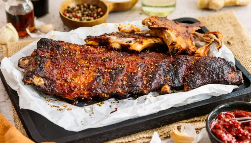 Saftige spareribs im backofen, glasiert und mit Gewürzen bestreut, serviert mit BBQ-Sauce.