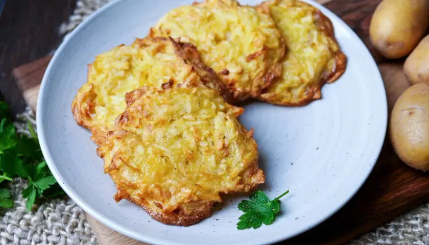 Goldbraune Kartoffelpuffer im Airfryer, knusprig und lecker, auf einem Teller mit Petersilie garniert.
