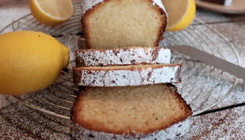 Zitronenkuchen wie bei Oma, mit Puderzucker bestäubt, neben frischen Zitronen auf einem Gitterrost.