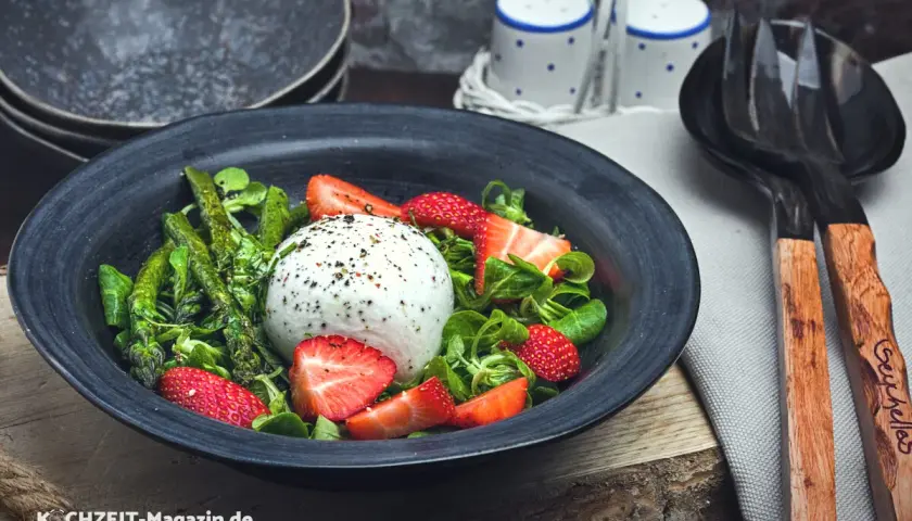 Ein frischer Spargelsalat mit Erdbeeren und Burrata, garniert mit Kräutern und Pfeffer.
