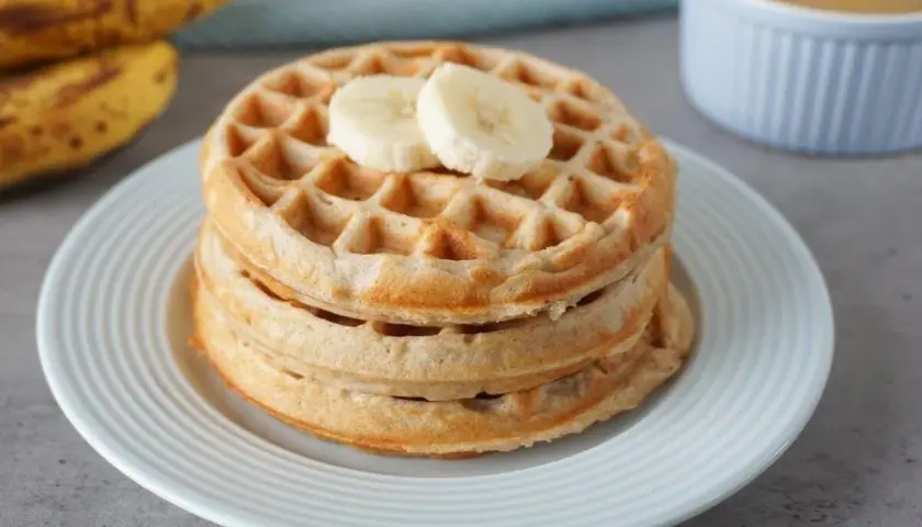 Stapel goldbrauner bananenwaffeln ohne zucker, garniert mit Bananenscheiben. Daneben liegen reife Bananen.