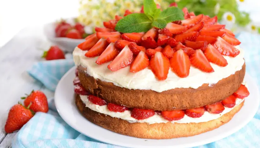 Eine zweistöckige Erdbeer-Sahne-Torte, üppig belegt mit frischen Erdbeerscheiben und garniert mit Minze.