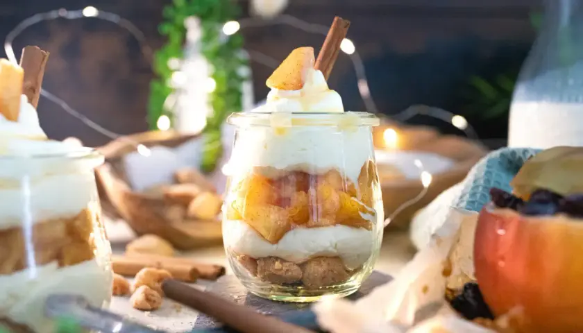 Leckeres Apfel-Crumble-Dessert im Glas mit Zimtstange und Sahne. Ein süßer Genuss, der zum Naschen einlädt.