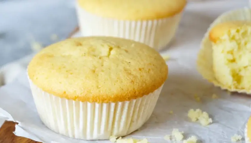 Frisch gebackene Vanille-Muffins, perfekt für ein einfaches Muffins Rezept. Einer ist angeschnitten und zeigt die saftige Krume.