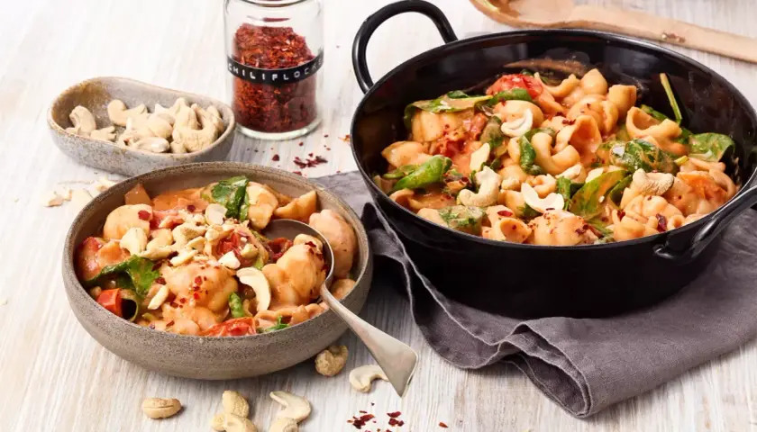 Ausgefallene Pasta-Rezepte vegetarisch: Cremige Muschelnudeln mit Cashews, Tomaten und Spinat, bestreut mit Chili-Flocken.