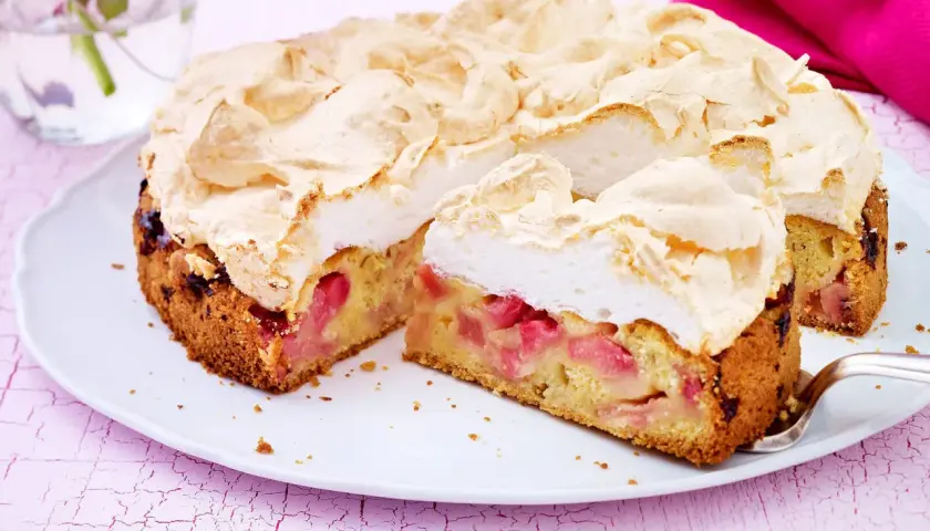 Ein saftiger Rhabarberkuchen mit einer luftigen Baiserhaube, auf einem weißen Teller angerichtet.