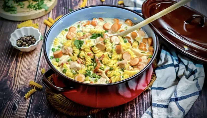 Herzhaftes Nudelgericht mit Würstchen, Erbsen und Hähnchen in cremiger Sauce. Köstliche gerichte mit sahne, garniert mit Petersilie.