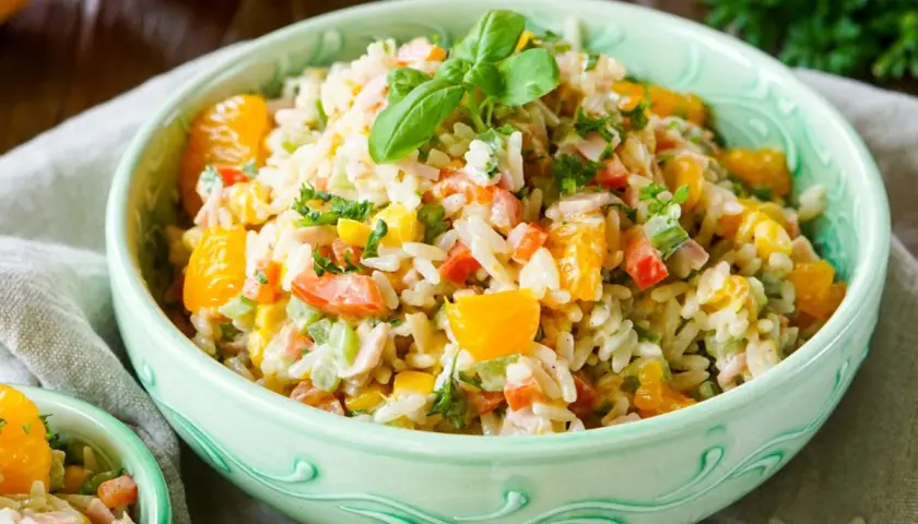Erfrischender Reissalat mit Mandarinen, Paprika, Mais und Kräutern, garniert mit Basilikum.