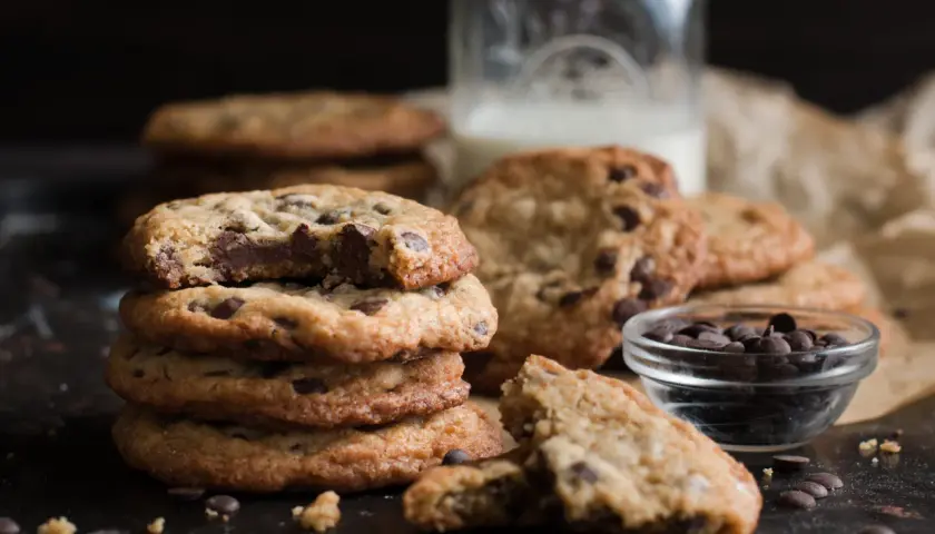 Ein Stapel saftiger Chocolate Chip Cookies, perfekt für ein einfaches Cookies Rezept. Daneben eine Schale Schokodrops und ein Glas Milch.
