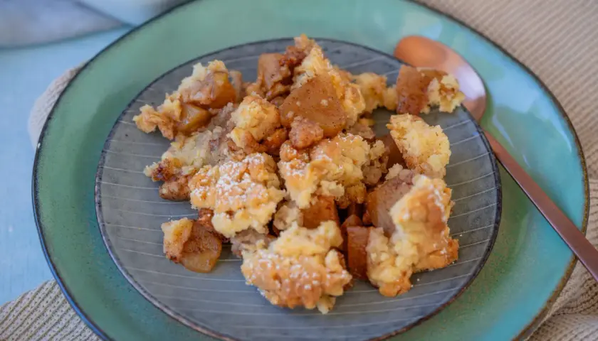 Ein Teller mit warmem Apfel Crumble, bestäubt mit Puderzucker. Die goldbraunen Apfelstücke und knusprigen Streusel laden zum Genießen ein.
