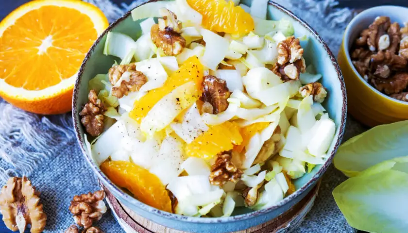 Erfrischender chicoree salat mit saftigen Orangenspalten und knackigen Walnüssen, garniert mit Pfeffer.