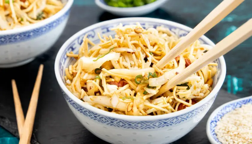 Ein Schüsselchen "friss dich dumm Salat" mit Nudeln, Gemüse und Mandeln, bereit zum Genießen mit Stäbchen.